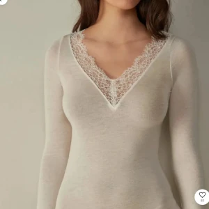 Vit långärmad topp med spets - Superfin vit långärmad topp med djup v-ringning och bred spetskant runt halsen. Sitter tight och har en mjuk, stretchig känsla. Perfekt att styla med jeans eller kjol för en clean look.