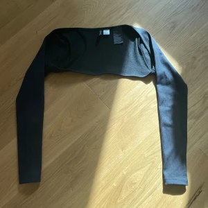 Bolero från Gina Tricot - Svart bolero från Gina Tricot med lång ärm och ribbad struktur. Toppen är croppad och sitter snyggt över axlarna, perfekt att slänga över ett linne eller klänning. Enkel och stilren design som funkar till många outfits.🫶🏼💗