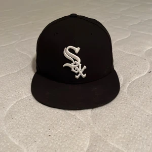 Svart White Sox keps New Era 59FIFTY - Snygg svart keps från New Era 59FIFTY med broderad White Sox-logga i vitt framtill och MLB-logga bak. Klassisk flat peak och stilren look, perfekt för dig som gillar sport och streetwear. Tillverkad i polyester och officiell MLB on-field cap.