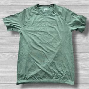 Grön t-shirt från Craft i storlek L - Snygg grön t-shirt från Craft i storlek L. T-shirten har rund halsringning och är tillverkad i ett mjukt och lätt material som passar perfekt för träning. Enkel design med diskret Craft-logga på bröstet och korta ärmar.
