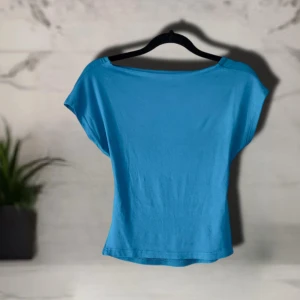 Turkos topp med urringning baktill - Snygg turkos med djup öppen ryggen. Modellen har korta ärmar och är tillverkad i mjuk bomull som känns skön mot huden. 