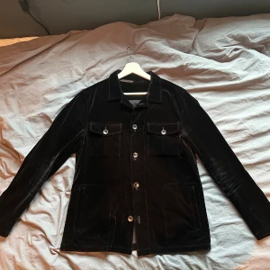 Svart Oscar Jacobson Overshirt (sammet) - Svart sammets-overshirt från Oscar Jacobson i strl M. Plagget är i bra skick men mindre tecken på användning finns. Nypris är 2999kr, men säljer nu för 699kr. Hör av er vid frågor eller funderingar! (Obs - Svårt att få rätt ljus på bild, t.ex har är inte ryggen den bruna färg som uppstår på bilden)