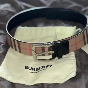Burberry Checked Buckle Belt - Snyggt bälte från Burberry med klassiskt rutigt mönster i beige, svart och rött. Bältet har en silverfärgad metallspänne och svarta skinn-detaljer vid spännet. Perfekt accessoar för att lyfta din outfit.
