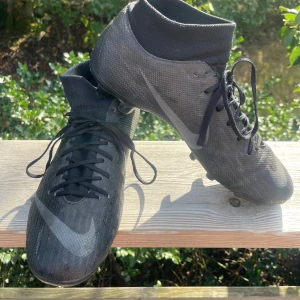 Svarta Nike fotbollsskor med snörning - Säljer ett par svarta Nike Mercurial Superfly Academy storlek 40,5 med dobbar för gräs och konstgräs (multiground, MG). 