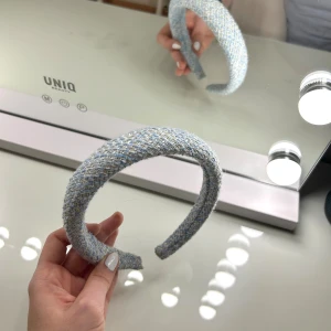 Blått tweeddiadem från DARK - Brett diadem i cool ljusblå tweed från DARK. Diademet har en vävd struktur med inslag av vitt och guld, vilket ger en lyxig och trendig känsla. Perfekt accessoar för att lyfta din look med en touch av klassisk stil.