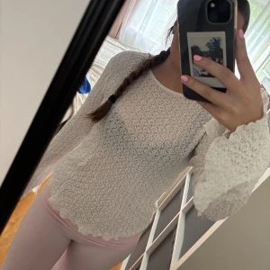 Vit blus med volangärmar - Säljer en söt vit blus med långärmade volangärmar och vågig kant nertill. Blusen är genombruten och har ett luftigt, stickat material som ger en romantisk känsla. Perfekt för dig som gillar en feminin och trendig stil.