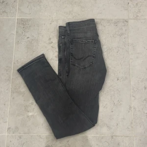 Svarta slim jeans Jack & Jones 29/30 - Slim fit jeans från Jack & Jones i tvättad svart färg. Modellen heter SLIM/GLENN och har klassisk femficksdesign, normal midja och smala ben. Jeansen är tillverkade i stretchig denim för extra komfort och snygg passform.
