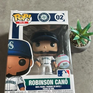 Funko Pop! MLB Robinson Canó #02 - Samlingsfigur Funko Pop! MLB Robinson Canó #02, Seattle Mariners. Figuren är i originalförpackning med tydliga MLB- och Funko-märkningar. Lådan har mindre slitage men är i gott skick. Perfekt för samlare och fans av baseball och Funko Pop!