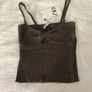 Linne med smala axelband  - Ett jättefint brunt linne med smala axelband och en detalj vid bröstet. Den är aldrig använd och har kvar prislappen 