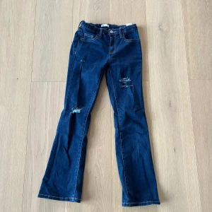 Mörkblå bootcut jeans med slitningar - Snygga mörkblå jeans med bootcut passform och slitna detaljer på benen. Jeansen är tillverkade i mjukt denimtyg.