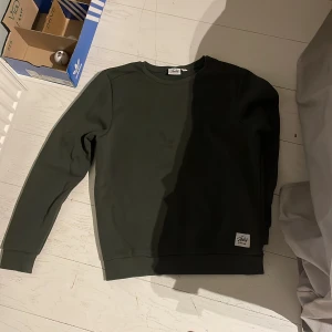 Mörkgrön sweatshirt från Andy by Frank Dandy - En stilren mörkgrön sweatshirt från Andy by Frank Dandy. Tröjan har rund hals, ribbade muddar vid ärmslut och nederkant samt en snygg logotyp-patch nertill. Perfekt för dig som gillar enkel och clean streetstyle.