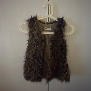 Brun pälsväst från H&M - Säljer en fluffig och trendig brun pälsväst från H&M. Västen har långa, mjuka fuskpälsstrån och är fodrad på insidan. Perfekt att slänga över en hoodie eller långärmad tröja för en cool lager-på-lager-look.