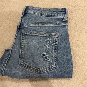 Blå jeansshorts med slitningar från H&M - Snygga blå jeansshorts från H&M med slitna detaljer och råa kanter. Klassisk femficksmodell med dragkedja och knapp framtill. Shortsen har en cool, avslappnad vibe och är perfekta för varma dagar.