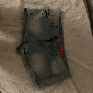 Ljusblå jeansshorts Stitch & Soul - Säljer ett par ljusblå jeansshorts från Stitch & Soul med slitna detaljer och råa kanter. Shortsen har flera fickor, bälteshällor och coola nitar vid ena fickan. Perfekta för en avslappnad och trendig look.