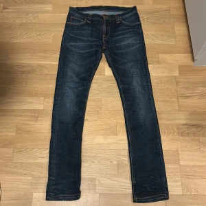 Nudie Jeans Tube Tom Gloom Blue 31/32 - Snygga mörkblå jeans från Nudie Jeans i modellen Tube Tom. Jeansen har klassisk femficksdesign, orangea kontrastsömmar och är tillverkade i 98% ekologisk bomull och 2% elastan för en bekväm stretch. Perfekt passform med smal siluett.