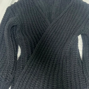 Svart omlottstickad kofta - Mysig svart stickad kofta med omlott-design och grov ribbad struktur. Perfekt för lager-på-lager och har lång ärm. Snygg och enkel att matcha med olika outfits.