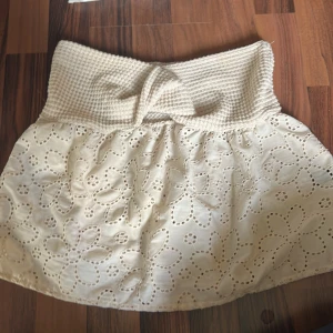 Tub topps liknande  - Supersöt beige tub topps liknande  från SHEIN med bred, stickad midja och knytdetalj framtill. Kjolen har broderade blommor i spets och är perfekt för en somrig look. Lätt och luftig modell som ger en romantisk vibe.