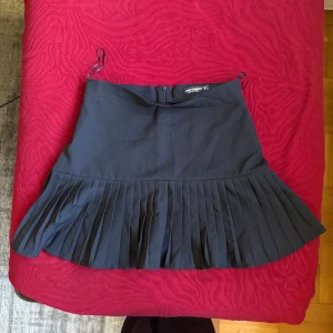 Svart plisserad kjol från Miss London - Snygg svart kortkjol från Miss London med breda plisserade veck nedtill. Kjolen har en enkel design med dragkedja bak och är perfekt för dig som gillar en stilren look. Tillverkad i ett mjukt och följsamt material. Står i storlek L men känns mer som en M.