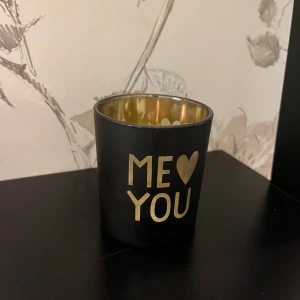 Ljuslykta - Bilderna visar en dekorativ ljushållare i svart och guld med texten 'ME ♥ YOU'.
