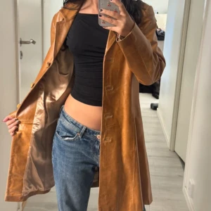 Brun skinnrock i klassisk modell - Snygg brun skinnrock med knappar framtill och slät finish. Jackan har en rak, något figursydd passform och är helfodrad med ett glansigt innerfoder. Perfekt för dig som vill ha en tidlös och cool look.