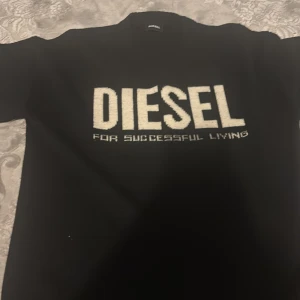 Svart tröja från Diesel med logga - Svart långärmad tröja från Diesel med stor vit logga och texten 'For Successful Living' på bröstet. Tillverkad i en mjuk blandning av ull och akryl, perfekt för dig som gillar streetwear och vill sticka ut med en tydlig logga.