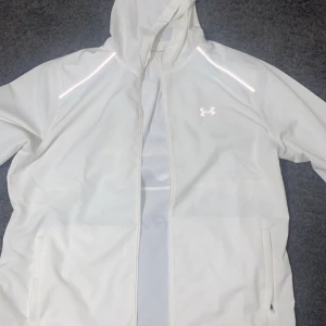 Vit vindjacka från Under Armour - Snygg vit vindjacka från Under Armour med huva och dragkedja  