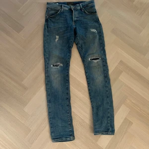 Blå slim fit jeans Jack & Jones - Säljer ett par blå slim fit jeans från Jack & Jones, modell Slim/Glenn. Jeansen har slitna detaljer och hål vid knäna för en cool look. Klassisk femficksmodell med normal midja och smal passform. Tillverkade i stretchig denim för extra komfort.