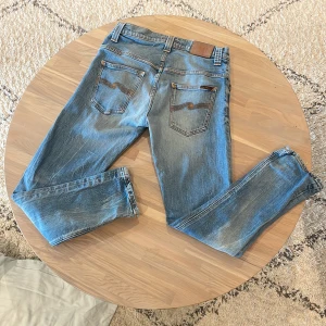 Blå jeans från Nudie Jeans Co - Snygga blå jeans från Nudie Jeans Co med klassisk femficksdesign och orange kontrastsömmar. Jeansen har raka ben och cool slitning på både fram- och baksida. Bakfickorna har Nudie Jeans signaturbrodyr. Perfekta för en avslappnad streetstil.