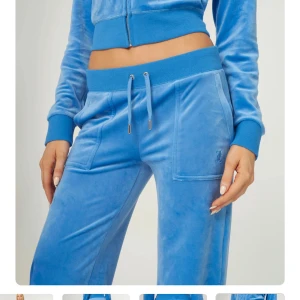 Blå velour mjukisbyxor med snörning - Snygga blå mjukisbyxor i mjuk velour med bred resår och snörning i midjan. Byxorna har raka ben med lätt utsvängd bootcut, stora fickor fram och bak med knappdetaljer. Perfekta för en chill och trendig look. Juicy Couture. Dem har varit uppsydda men har sprättat upp dem.