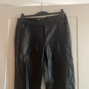 Svarta skinnbyxor från BikBok - Snygga svarta byxor i skinnimitation från BikBok med raka ben,  fickor både fram och bak. Använda 1 gång