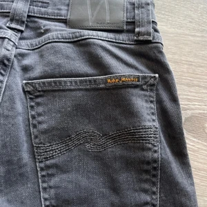 Svarta skinny jeans från Nudie Jeans - Säljer ett par svarta skinny jeans från Nudie Jeans i storlek W27 L32. Jeansen har klassisk femficksdesign, svarta sömmar och Nudie-logga på bakfickan. Snygg passform med smala ben och tillverkade i mjukt jeanstyg. Kan diskutera priset 