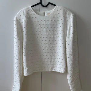 Vit pärlprydd tröja från H&M - Superfin vit långärmad tröja från H&M med pärldetaljer över hela plagget. Tröjan har rund halsringning och knäppning bak i nacken. Perfekt för dig som vill sticka ut med en elegant och trendig look.