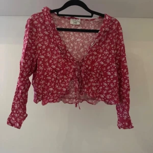 Mörkrosa blommig blus med snörning - Supersöt mörkrosa blus från NA-KD med vita småblommor och croppad passform. Djup v-ringning med volangkant och snörning framtill. Blusen är aldrig använd men saknar tyvärr prislapp.