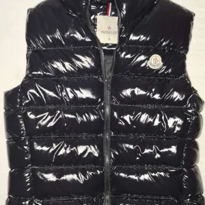 Svart dunväst från Moncler - Snygg svart dunväst från Moncler med glansig finish och klassisk logga på bröstet. Västen har quiltad design, dragkedja framtill och är fodrad med mjukt material. Perfekt för lager-på-lager och streetstyle.