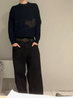 Mörkblå stickad tröja  - Mörkblå stickad tröja med gröna detaljer och ett broderat motiv av en bil på bröstet. Rund halsringning med färgade ränder och långa ärmar. Materialet är 50% ull och 50% syntet, perfekt för kyligare dagar.