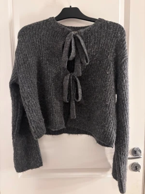 Grå stickad tröja med knyt från Gina Tricot - Mysig grå stickad tröja från Gina Tricot med två dekorativa knytband där fram. Man kan göra den tajtare eller större ifall den är för liten/stor. PS! Om du köper innan kl 17 postar jag det samma dag🥰