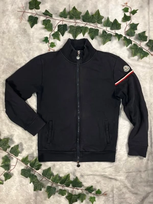 Moncler Maglia Cardigan Zip – Mörkgrå – Strl S - |Färg: Mörkgrå/charcoal, tricolour-detalj | Modell: Maglia Cardigan Zip | Storlek: S, slim–normal passform | Skick: Grade C+, 7/10 (litet hål, rost på dragkedja) | Hör av dig ifall du har funderingar!