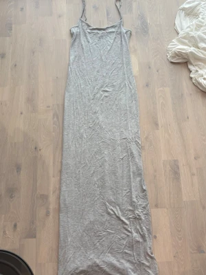 Grå långklänning från Gina Tricot - Lång, smal grå klänning från Gina Tricot med tunna axelband och enkel design. Tillverkad i mjuk bomullsmix som känns skön mot huden. Perfekt för en avslappnad och stilren look.