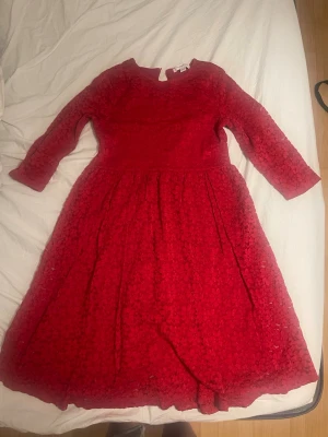 Röd blommig klänning med trekvartsärm - Röd klänning med blommigt mönster och trekvartsärm. Klänningen har rund halsringning och är tillverkad i ett tyg med struktur. Kjolen är utsvängd och längden går till knäna. Perfekt för dig som vill sticka ut med färg och mönster. Tveka inte på att höra av dig om du har några frågor 