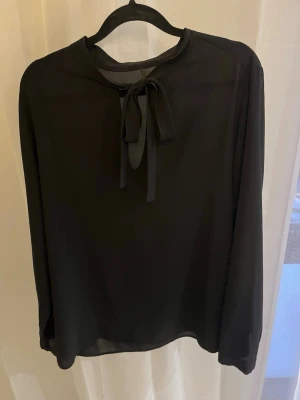 Svart blus med knytband i halsen - Svart blus med långa ärmar och knytband i halsen. 