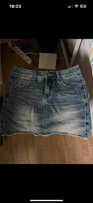 Blå jeanskjol - Säljer en klassisk blå jeanskjol i kort modell med slitna detaljer och rå, fransig kant nedtill. Storlek XXS/XS! Den sitter low waist!