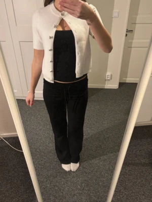 Vit kortärmad kofta från Zara - Kortärmad vit kofta från Zara med rund halsringning och dekorativa silvriga knappar framtill. Koftan är stickad i mjukt material och har en rak, något kortare passform. Perfekt att styla över ett linne eller t-shirt.