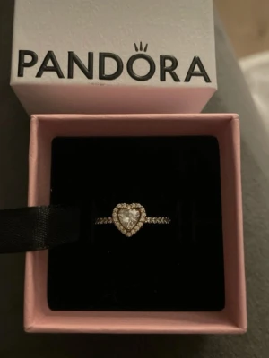 Pandora ring med hjärtformad sten - Superfin ring från Pandora i guld med hjärtformad  sten och små stenar runt om och längs ringen. Perfekt som promsie ring eller vardagligt bruk 🥰
