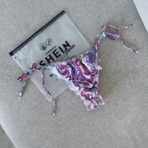 Lila mönstrad bikiniunderdel från SHEIN, strlk S - Helt ny och oanvänd lila bikiniunderdel med mönster från SHEIN i storlek S. Den har knytning i sidorna vilket gör den justerbar i midjan för optimal passform. Ett stilrent och somrigt plagg som passar perfekt för strand eller pool. Köptes för nypris 109kr! FÖRST TILL KVARN! Mått ➙