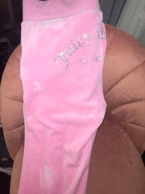 Rosa velourbyxor från Juicy Couture NYA - Säljer ett par ikoniska rosa mjukisbyxor från Juicy Couture i mjuk velour. Byxorna har glittrande Juicy-logga och JC-detaljer i strass på ena benet och bakfickan. Perfekta för dig som vill ha den klassiska Y2K-looken.