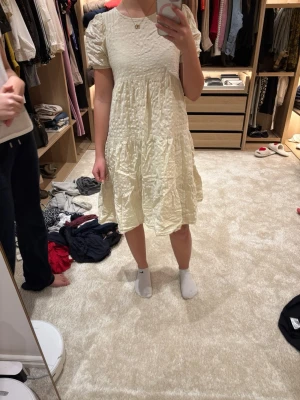 Ljus kortklänning från Lindex - Supersöt ljus kortklänning från Lindex med puffärmar och strukturerat tyg. Klänningen har en volangig kjol och rund halsringning. Perfekt för sommarens alla tillfällen och enkel att styla med sneakers eller sandaler.