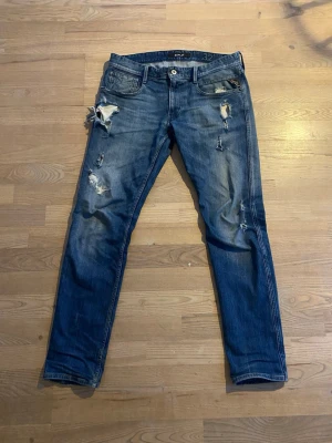 Replay Anbass - Säljer ett par blå skinny jeans med slitningar och hål på framsidan. Jeansen har klassisk femficksmodell, låg midja och är tillverkade i bomull med en snygg tvättad look. Perfekta för dig som gillar en avslappnad och trendig stil. Storlek:32/32