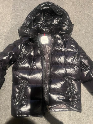 Svart glansig dunjacka från Moncler - Snygg svart dunjacka från Moncler med glansig finish och huva. Jackan har två framfickor med dragkedja och quiltad design. Perfekt för kalla dagar och ger en riktigt trendig look. Knappt använt så i princip nyskick. Nypriset är runt 15.000kr. Hör gärna av er vid frågor💘💘