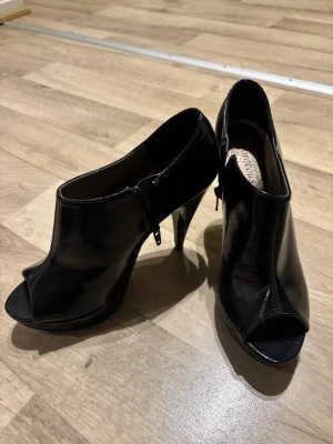 Vintage klackar från Gorgeous - Snygga svarta pumps från Gorgeous med öppen tå och hög klack. Skorna är tillverkade i glansigt skinnliknande material och har dragkedja på sidan för enkel påtagning. Perfekta för dig som vill ha en elegant och trendig look.