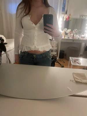 Vit ribbad topp med knappar NLY Trend XS - Vit ribbad topp från NLY Trend i storlek XS. Modellen har långa ärmar, v-ringning och silverfärgade knappar framtill. Tunt och stretchigt material som sitter snyggt på kroppen. 